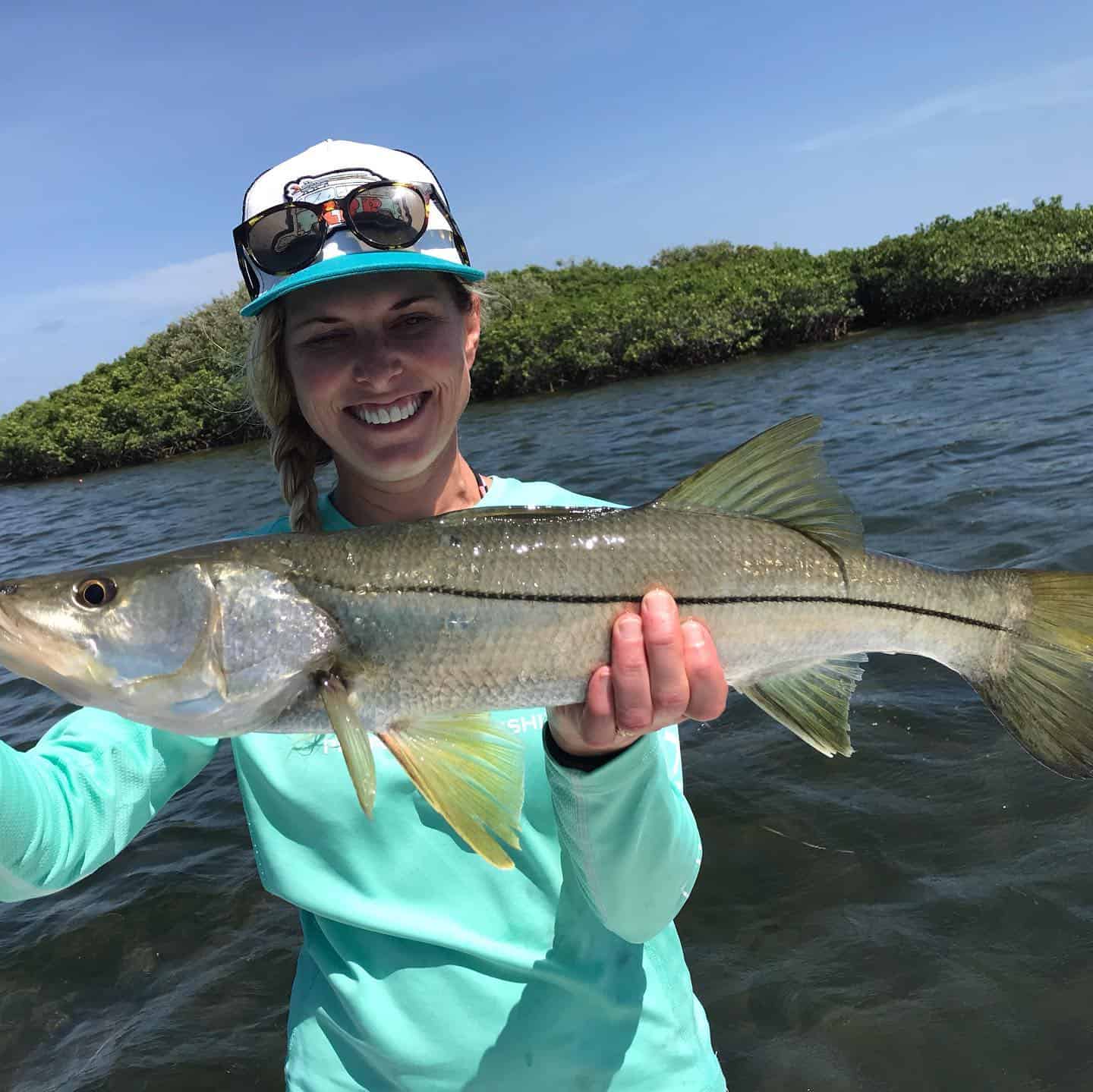 Woman holding up a Snook she caught while on an inshore fishing charter.