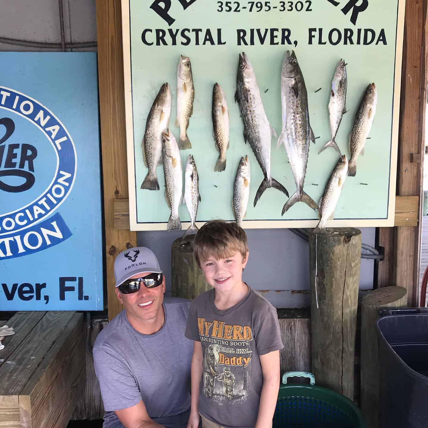 Father and son standing in front of a wall with fish pinned behind them.