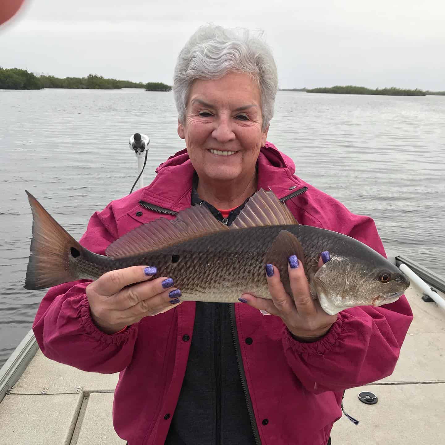 Woman wearing a pink jacket holding up a redfish while fall fishing in Crystal River, FL.