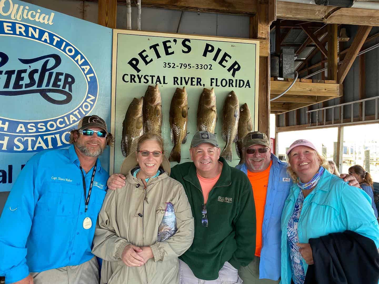 A group of friends and a fishing charter captain standing in front of a board of fish.
