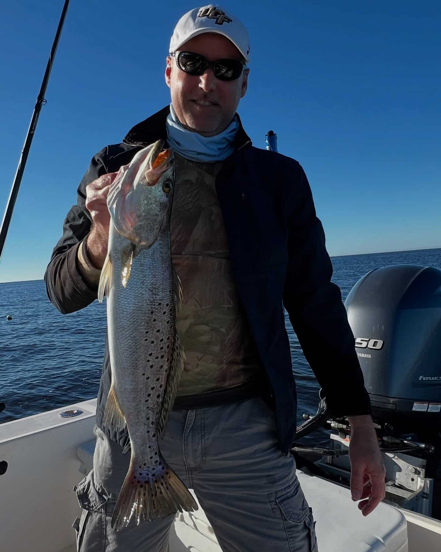 Man on a boat holding up a speckled trout he caught.