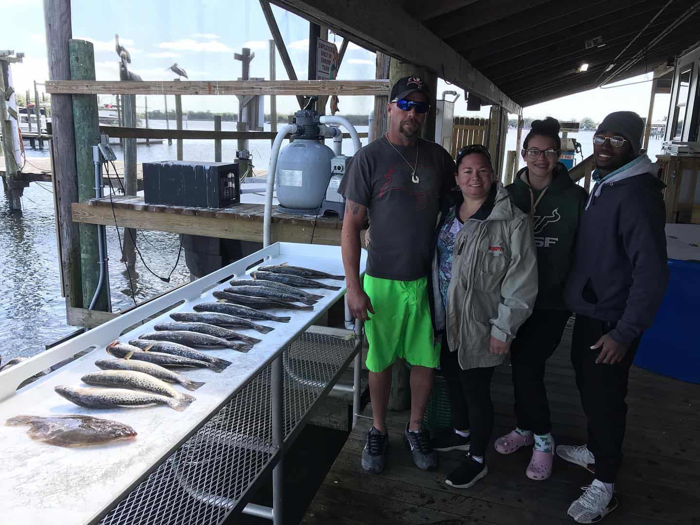 Group of people standing next to a table of fish they caught.