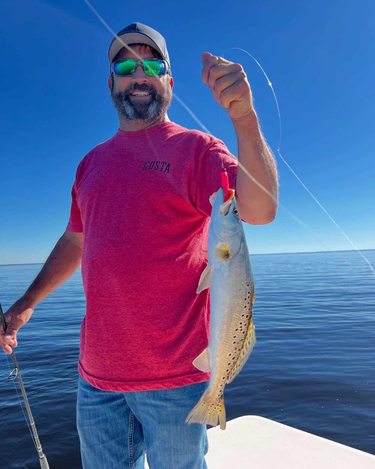 Man in a red shirt holding up a speckled trout.