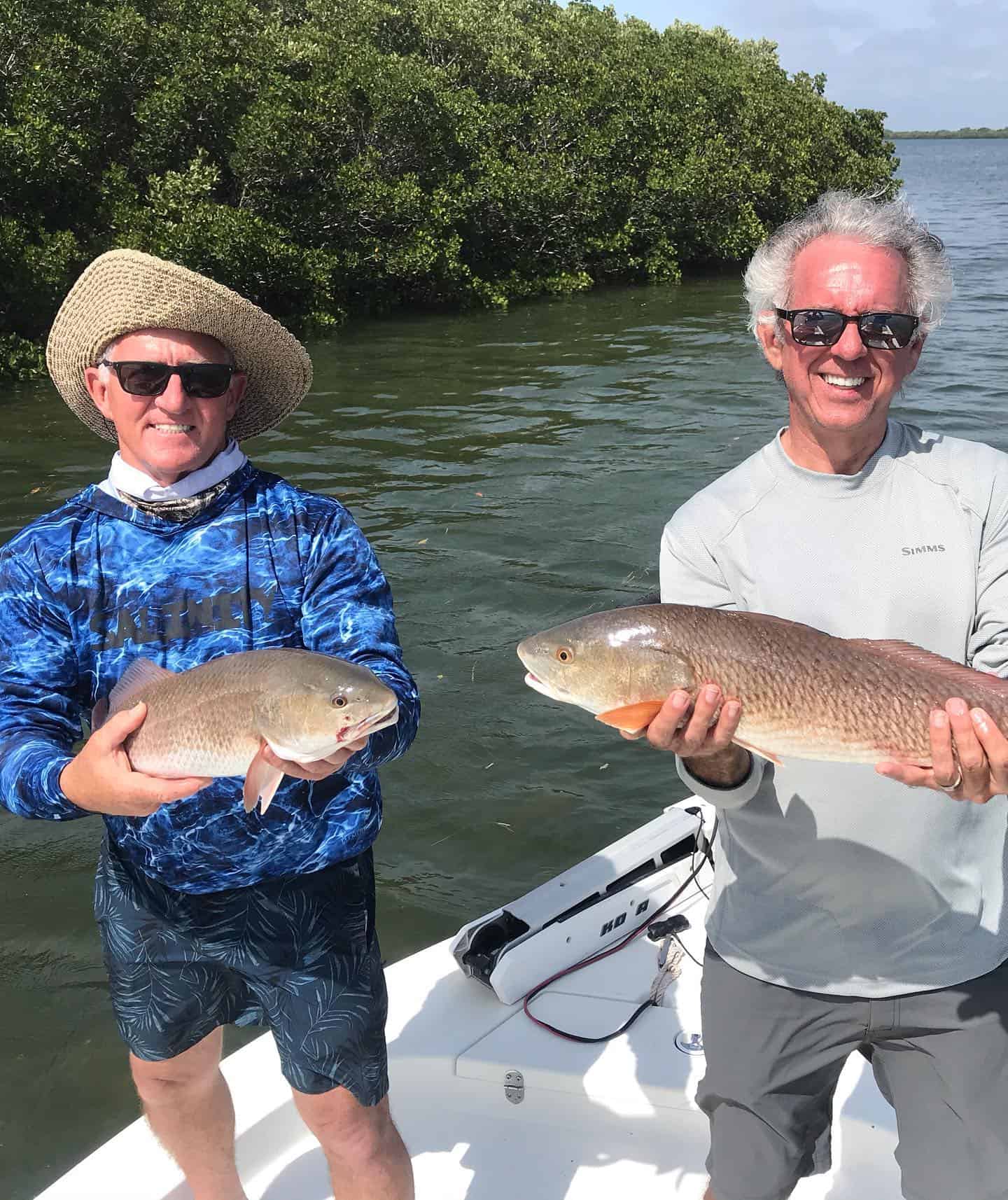 Two smiling anglers holding freshly caught redfish on a boat in Crystal River, Florida, with lush mangroves and calm waters in the background.